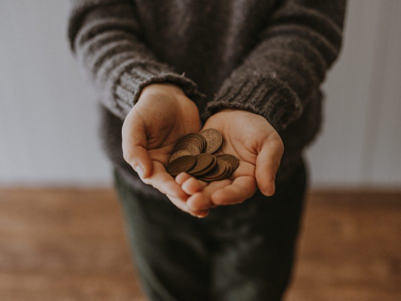 A person extends their hands, holding several coins