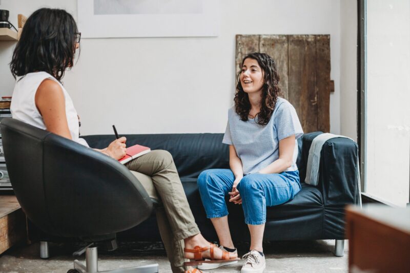 Young woman sits on a sofa talking to a therapist.