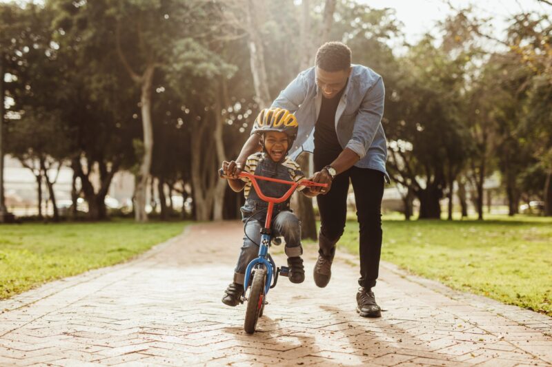 Boy learning to ride a bicycle with his father in park.
