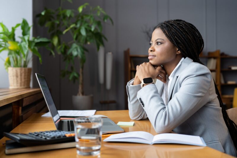 Woman pastor at desk with laptop looking out window