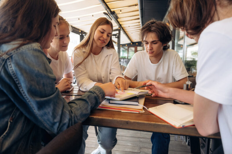 Learning group of teens sitting at table discussing a book