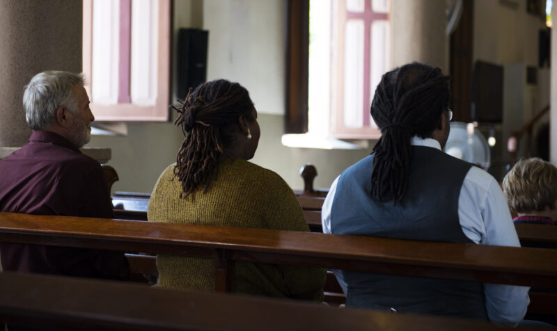 Three adults in wooden pew at local church