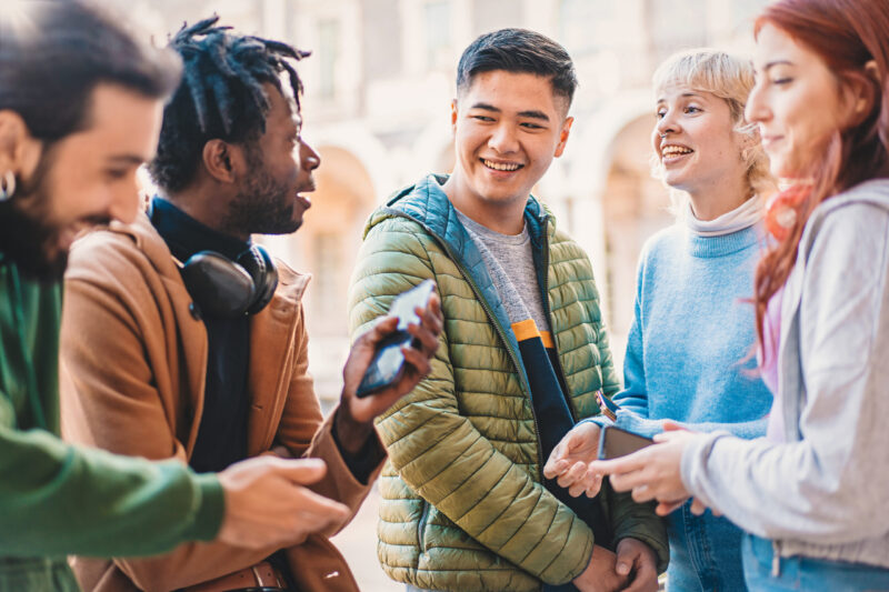 Group of diverse young adults smiling and engaging with smartphones in an outdoor courtyard